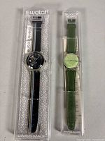 Both Swatch watches in clear plastic boxes