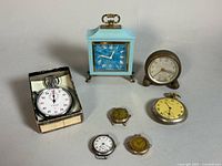 Group shot of stopwatch in box, two alarm clocks, pocket watch, three wristwatch heads