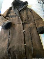 Full front view of dark brown shearling hooded coat showing buttons and unfinished hem