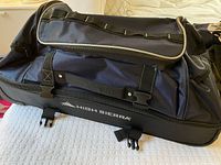 Overall view of navy and black High Sierra wheeled duffel showing exterior pockets, straps and logo