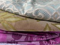 Stack of three patterned fabric pieces showing blue trellis, beige leaf, and magenta damask designs
