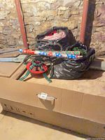 Box containing disassembled artificial tree, metal stand placed on top, roll of wrapping paper visible