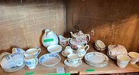 Shelf view of entire lot showing Coalport blue frieze pieces, white bud vase, Royal Doulton rose tea set, Paragon plates, pastel cups and saucers.