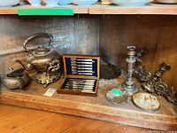 Cabinet shelf showing teapot, stand, flatware box, candlestick, candelabra, trays and dish