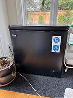 Front view of black Danby chest freezer with stickers and power cord