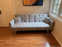 Front view of grey tufted futon sofa with two pillows