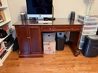 Front view of wood desk showing cabinet doors, drawer and open kneehole