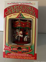 Front of boxed electronic carousel showing figures through display window