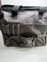 Front view showing dark gray tote, six exterior pockets, top zipper, webbing handles