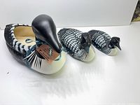 Three painted loon figures side by side showing relative sizes and materials