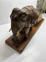 Side view of teak elephant on base, brass tusks visible