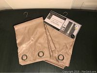 Photo of two beige curtain panels folded with metal grommets visible and original packaging card showing an example of the curtains in use.