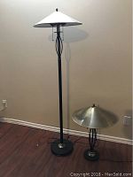 Pair of lamps including a taller floor lamp with white shade and a shorter table lamp with brass shade, both with black metal bodies and decorative midsections.