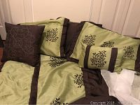 Photo showing green and brown double bed bedding set with bedspread, skirt, and five pillows featuring leaf embroidery.
