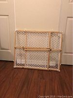 Folded Safety First baby gate with white plastic mesh and wooden frame photographed against a white door.