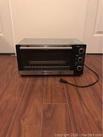 Photo of Hamilton Beach toaster oven on wood floor showing front and controls