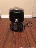 Front view of black Hamilton Beach Slushie Machine with clear container and lid, power cord visible.