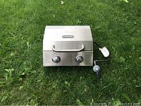 Closed tabletop propane grill by NXR showing front with two control knobs and propane connection hose and regulator attached.