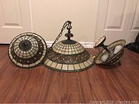 Photo of three stained glass ceiling lamps on a wooden floor, showing one large hanging lamp and two smaller lamps.