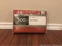 Photo of packaged fitted bed sheet in rusty red color with information label showing 300 thread count, double bed size, and other details.