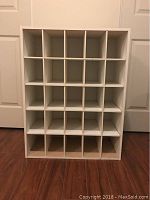 White wooden rack with 25 cubbies on a hardwood floor against white doors.