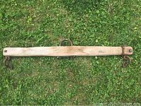 Photo showing the full length of the vintage wooden yoke with metal hooks at each end and an iron ring in the center, lying on grass.