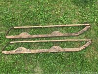 Pair of vintage sled skies laid out on grass, showing wooden base with metal frame sides, both exhibiting wear and aging.