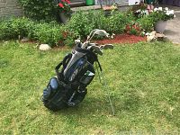 Photo shows an Adams branded navy blue and black golf bag with shoulder straps and retractable legs standing on grass. Set of 11 right handed ladies golf clubs is visible inside the bag, with club heads showing varied types including irons and a putter.