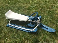 Blue GT winter sled with white plastic seat and steering wheel on grass