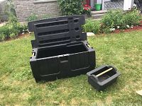 Heavy duty black plastic storage bench with lid open showing interior compartment and removable tray beside it on grass.