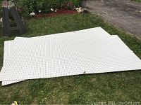 Photo showing two large white wooden pegboards laid flat on grass, each with evenly spaced holes for pegs, approximately 96 by 48 inches in size.