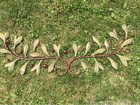 Photograph of metal wall hanging showing close-up of a vine shaped with metal leaves and berries on a grass background.