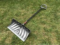 Grey metal and plastic snow shovel laid flat on grass showing straight handle and scoop