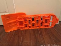 Orange plastic shovel and traction aid mat showing the flat shovel blade and textured traction aid