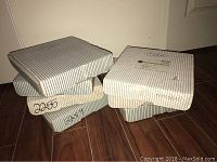 Stack of five rectangular white boxes with black stripes containing collector plates in original packaging.