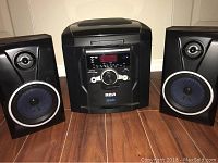 Set of RCA 5 CD changer stereo system with two black speakers on either side on a wooden floor.