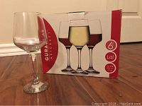 Photo of one clear wine glass next to the original box showing the set of six 10 oz glasses by Gurallar Artcraft