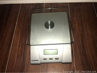 Photo of the Starfrit digital kitchen scale with a stainless steel platform, glass cover, and control buttons underneath the digital LCD display.