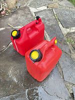 Two red plastic gasoline containers on stone surface showing overall appearance