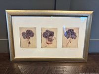 Overall view of three-panel hydrangea print framed in gold-toned wooden frame behind glass