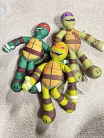 Front view of all three TMNT plush toys lying on carpet