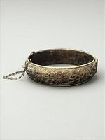Closed bangle showing engraved floral exterior and safety chain