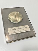 Reverse side of medal in holder showing stylized wing over globe and label