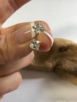 Close-up of both square CZ studs held between fingers