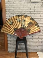 Full view of opened gold Japanese wall fan on stool