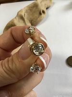 Three gold single stud earrings shown against driftwood for scale