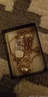 Necklace in box showing chain, pendant with faux pearl, and attached tag