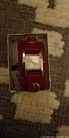 Guess watch in box showing rectangular case, red cuff strap, white dial