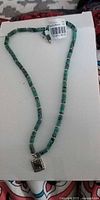 Full view of green bead necklace with square pendant and tag