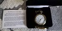 Open pocket watch showing white dial inside presentation box with booklet